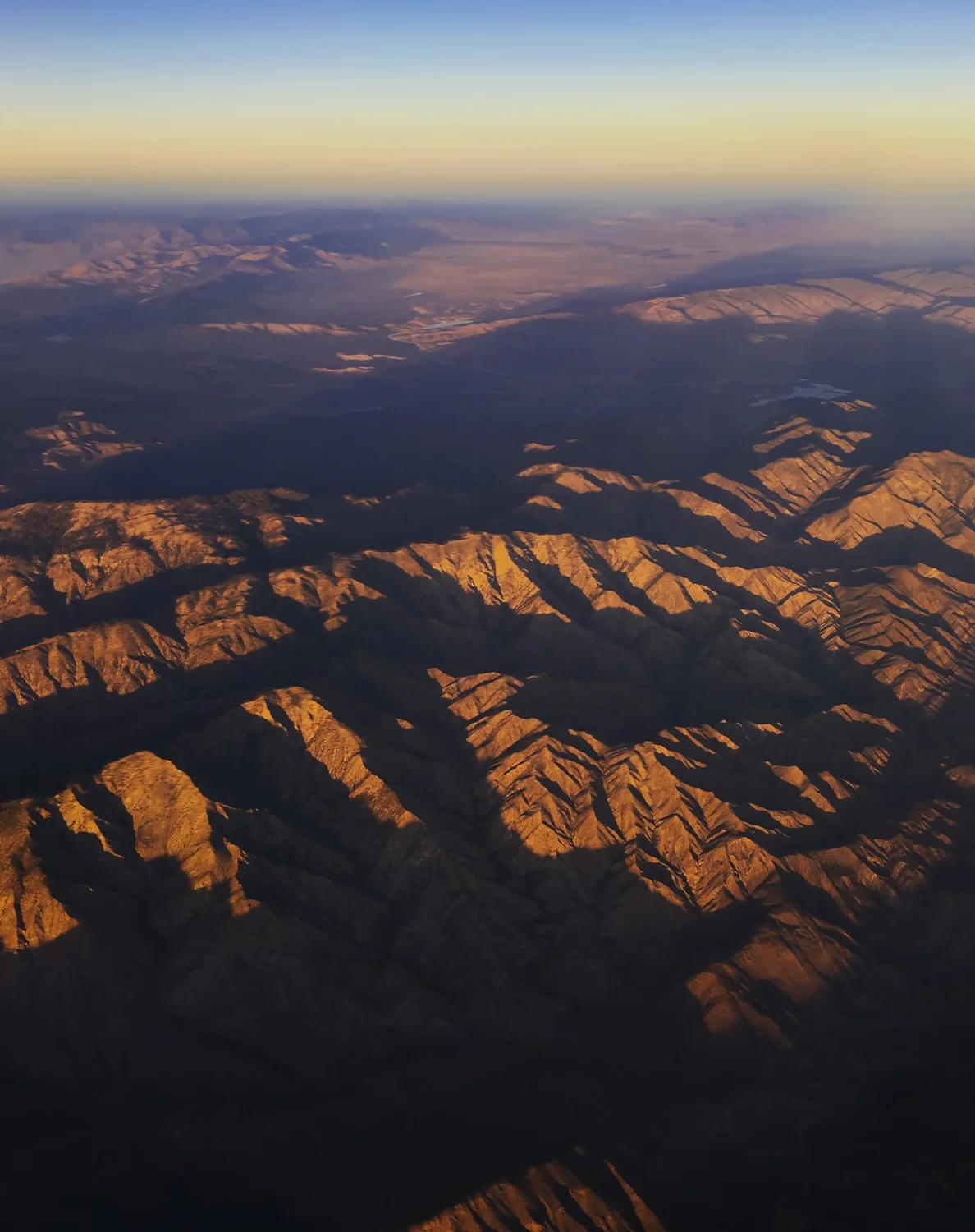 A picture from the air looking down on rugged mountains painted golden by the sunlight.