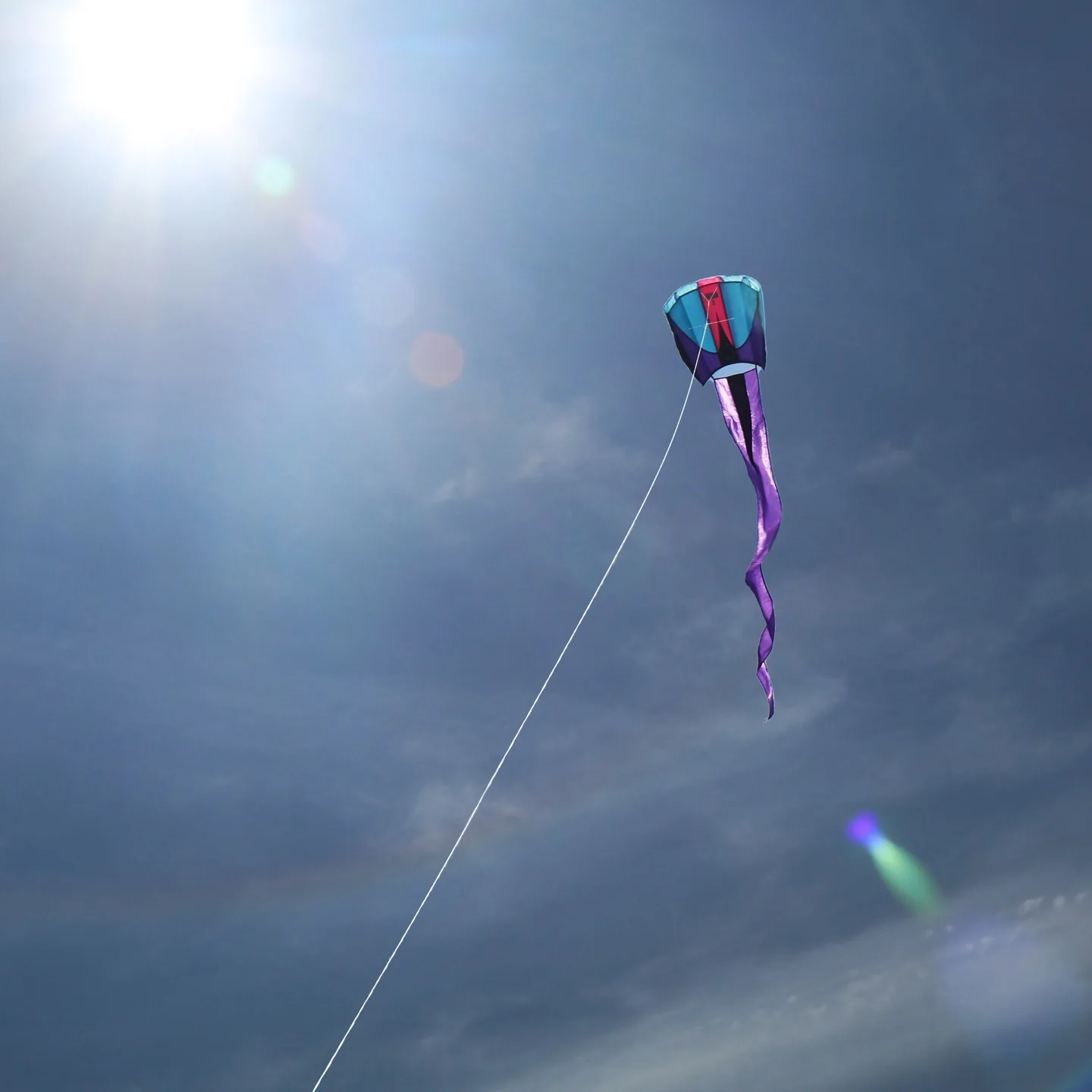 A kite flying in a blues sky with bright sun and few clouds.