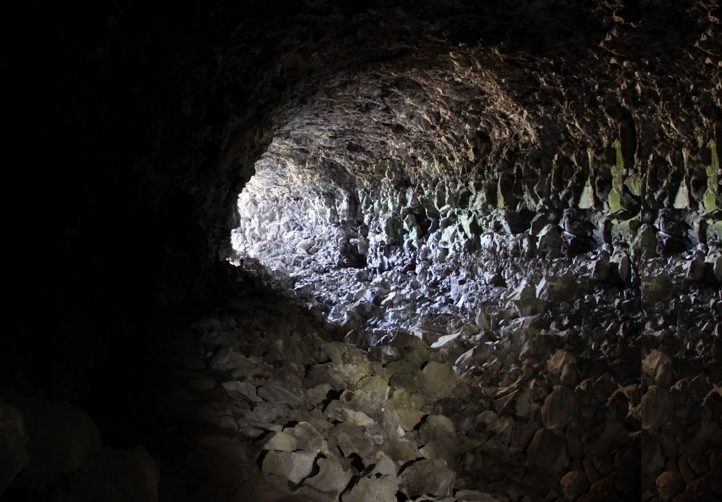 A lave tube cave, viewed from inside looking out to the light. A tiny person is barely visible, indicating the immense scale of the cave.