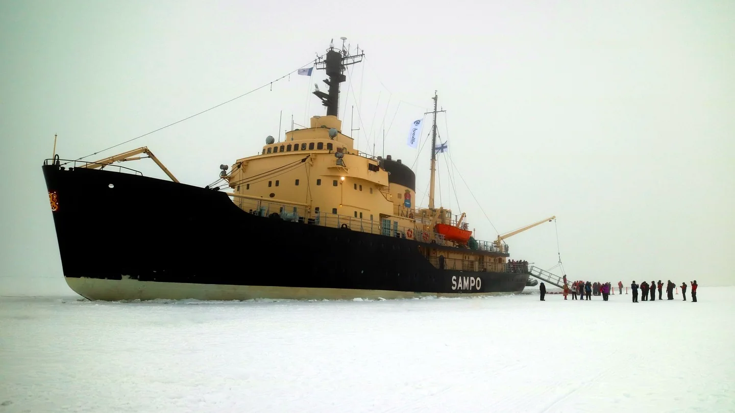 An ice-breaker ship out on a frozen sea. People are standing on the ice near the ship.