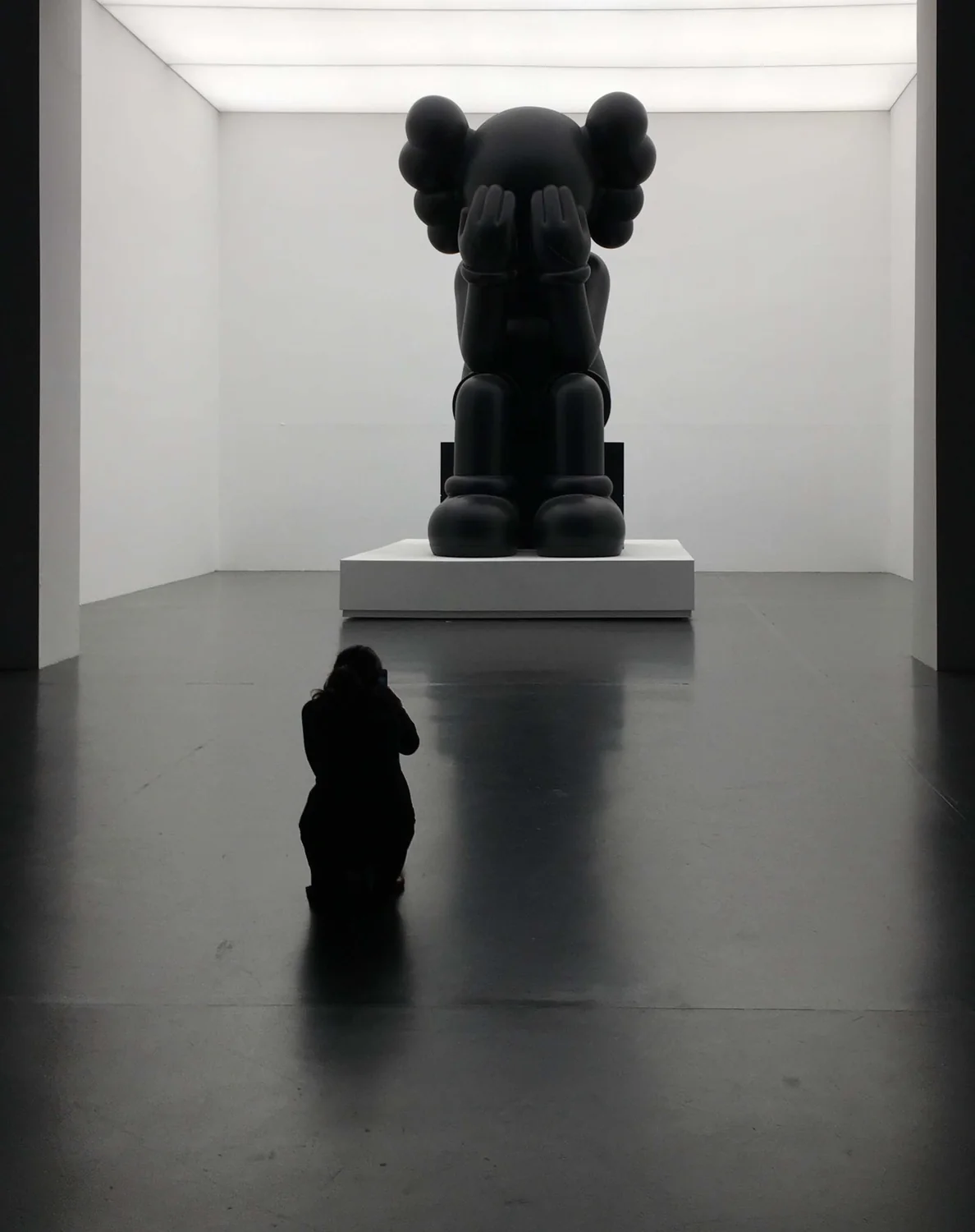 A woman taking a photo of a Kaws sculpture.
