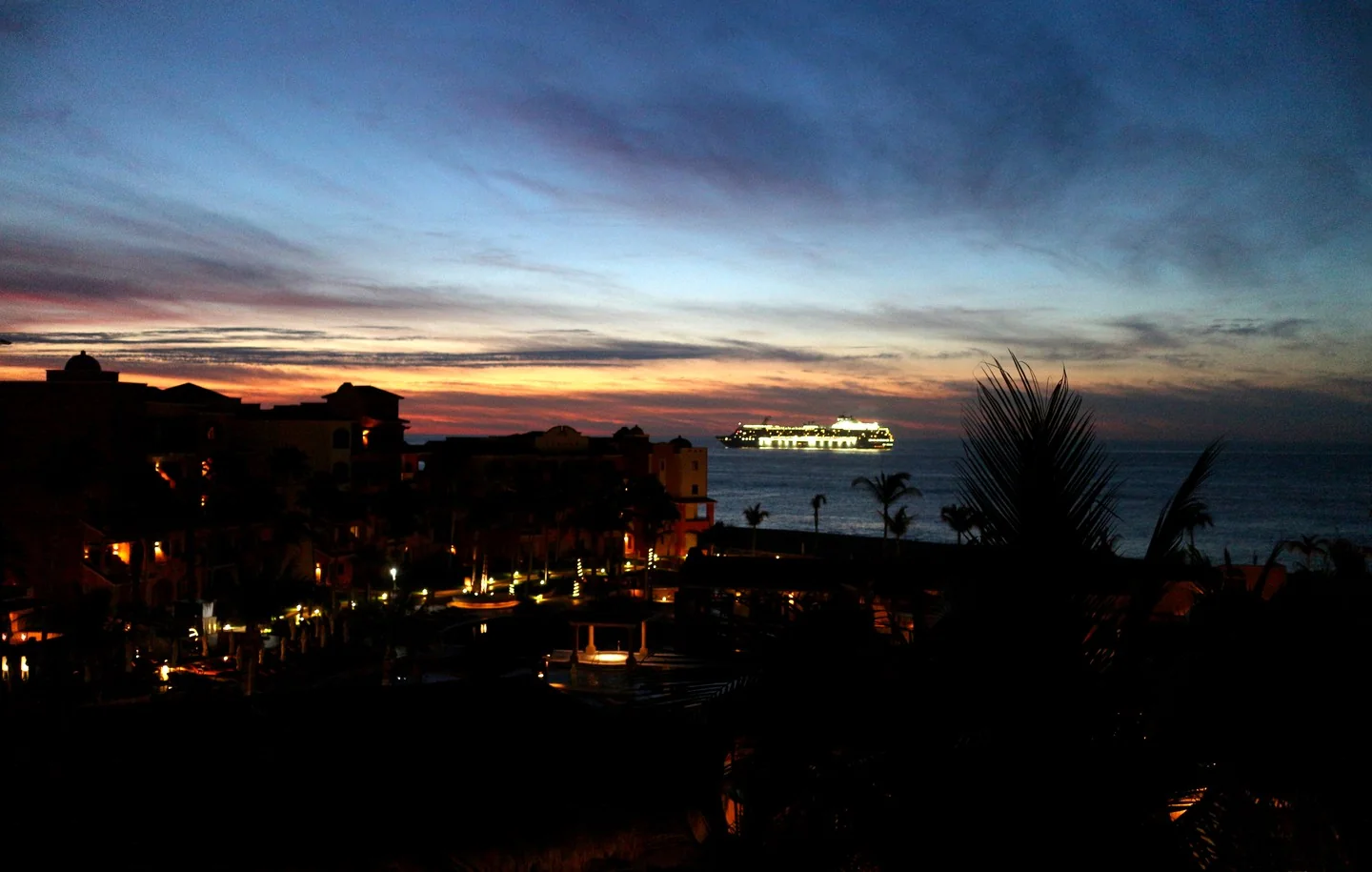 A cruise ship at night, with bright lights and colorful sky.