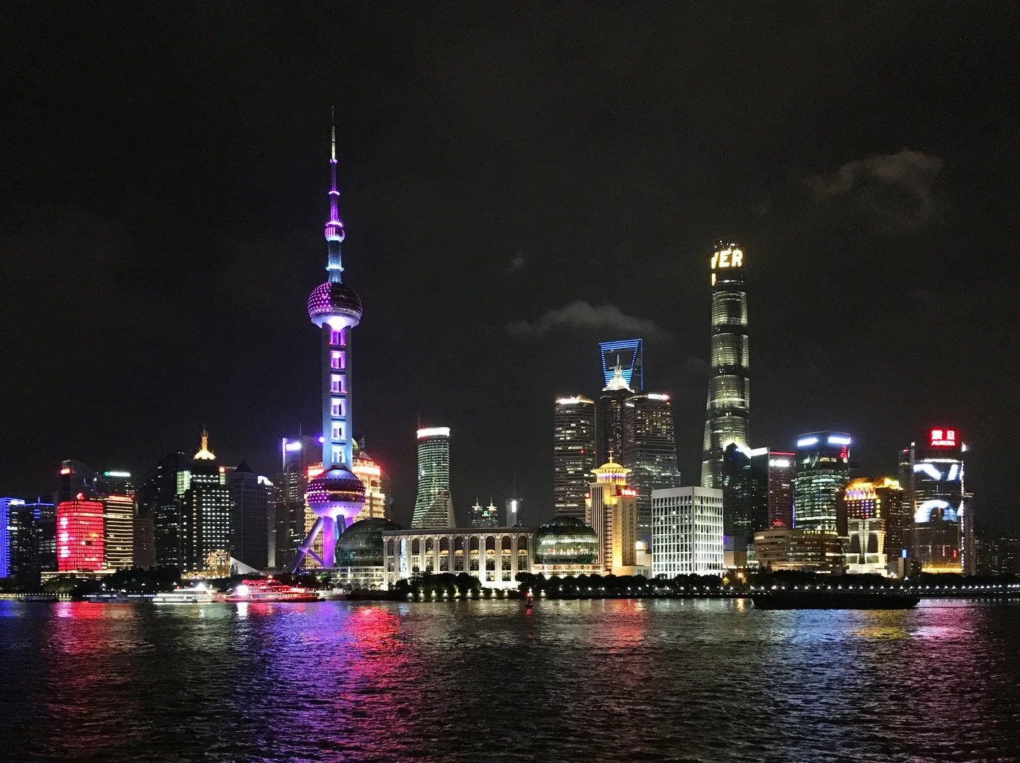 Tall buildings at night, bright colorful lights, viewed from across the water.