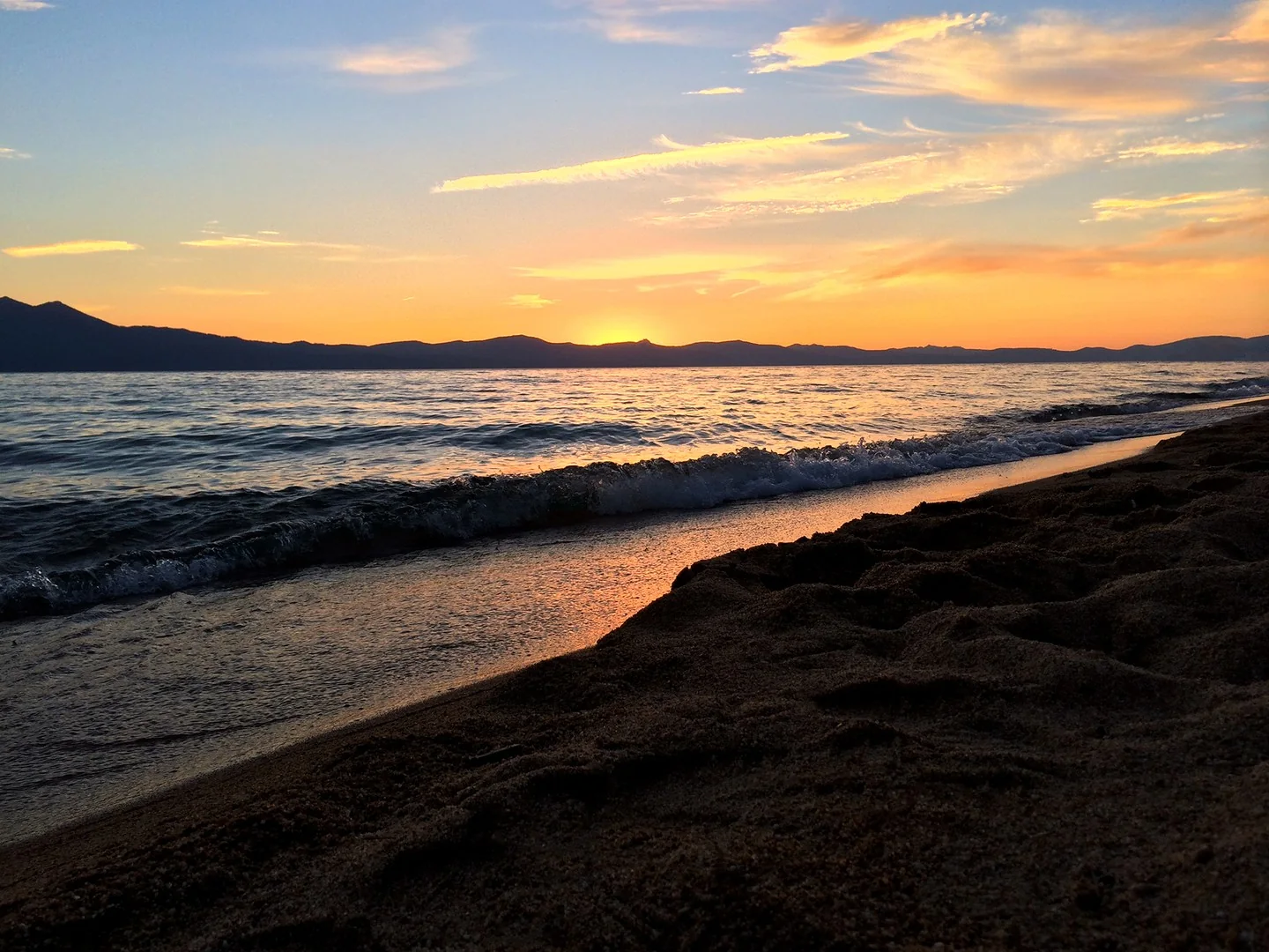 Sunsetting over a lake, behind mountains.