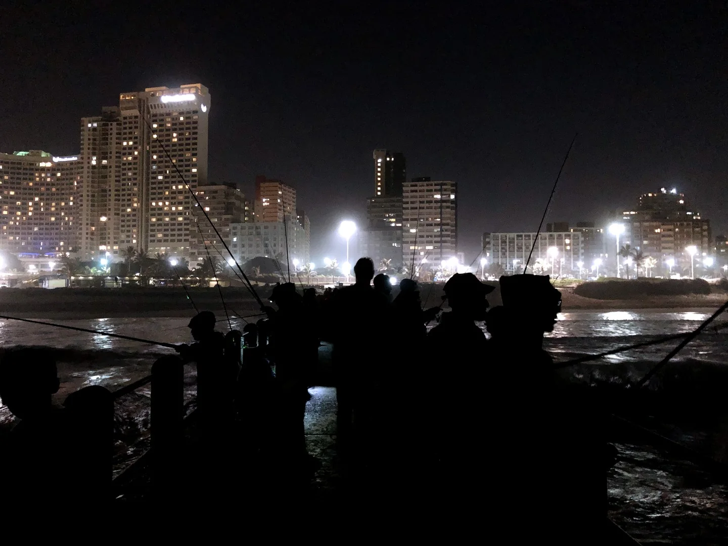 A group of people fishing from a pier at night in Durban.