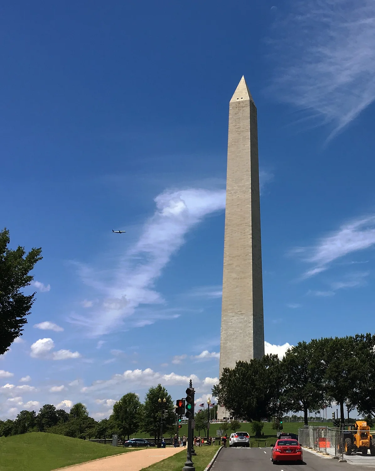 A photo of the Washington Monument against a blue sky. There is an airplane in the sky.